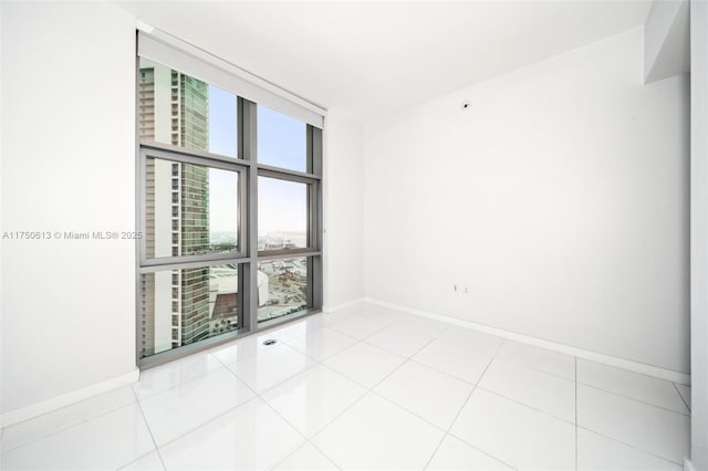 unfurnished room featuring a wall of windows, light tile patterned flooring, and baseboards