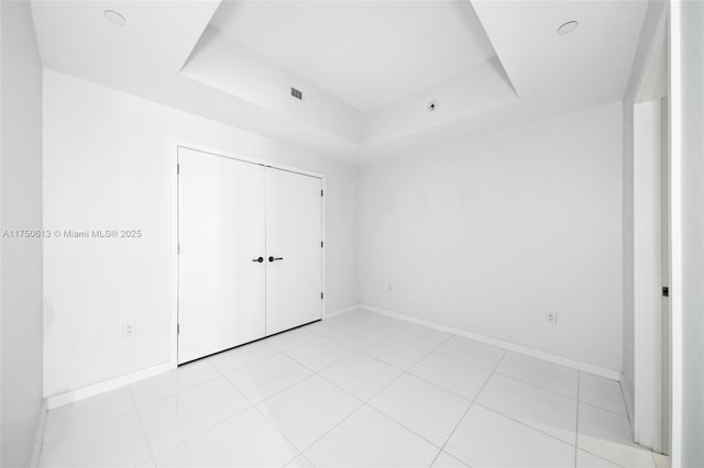 unfurnished bedroom with a tray ceiling, a closet, and baseboards