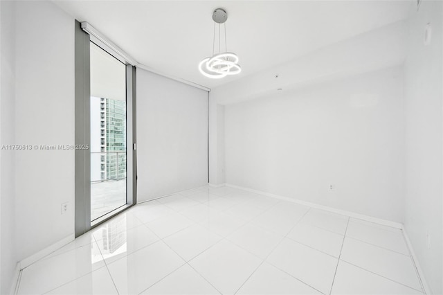 empty room featuring light tile patterned floors, baseboards, a wall of windows, and a chandelier