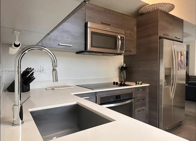 kitchen with appliances with stainless steel finishes, light countertops, a sink, and dark brown cabinets