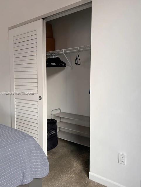 bedroom featuring concrete flooring, a closet, and baseboards