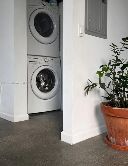 clothes washing area featuring stacked washing maching and dryer, baseboards, electric panel, and laundry area