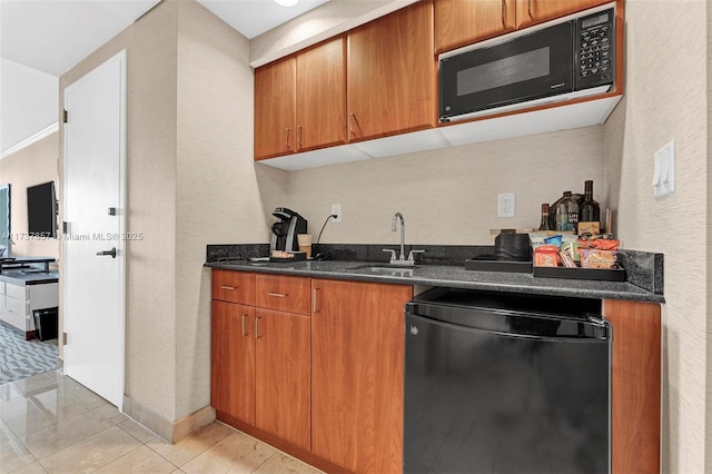 kitchen featuring brown cabinets, light tile patterned floors, a sink, dark stone countertops, and black appliances