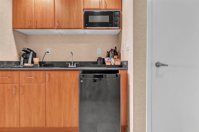 kitchen with brown cabinetry, dark stone counters, a sink, and black appliances