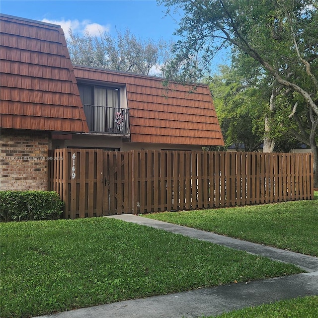 view of home's exterior with brick siding, a lawn, fence, and mansard roof