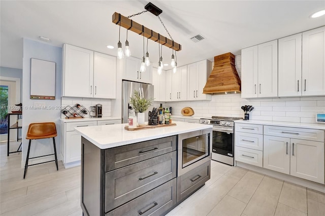 kitchen featuring custom range hood, decorative light fixtures, stainless steel appliances, light countertops, and white cabinetry