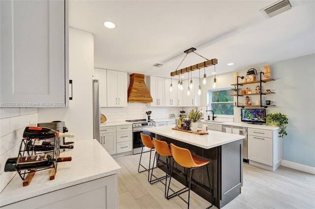 kitchen featuring a breakfast bar, stainless steel appliances, white cabinetry, a kitchen island, and premium range hood