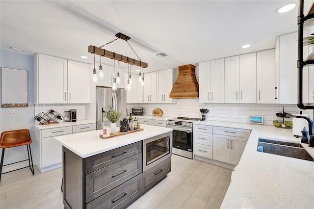 kitchen featuring a sink, white cabinetry, appliances with stainless steel finishes, custom exhaust hood, and decorative light fixtures