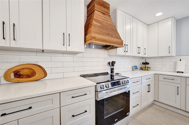 kitchen with tasteful backsplash, light stone countertops, custom exhaust hood, stainless steel range with electric stovetop, and white cabinetry