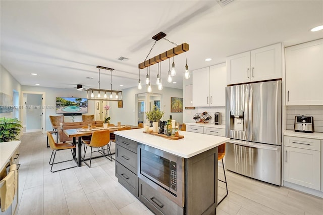 kitchen with stainless steel fridge, built in microwave, light countertops, white cabinetry, and pendant lighting