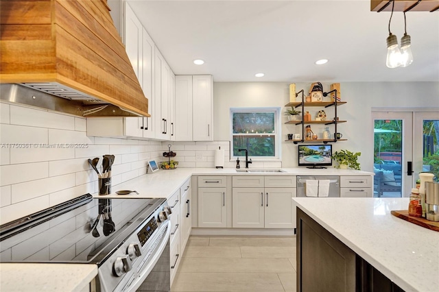 kitchen with custom range hood, appliances with stainless steel finishes, hanging light fixtures, white cabinetry, and a sink