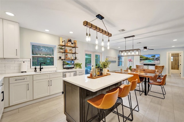 kitchen featuring pendant lighting, light countertops, visible vents, a kitchen island, and a sink