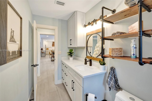 bathroom with toilet, visible vents, wood finish floors, and vanity