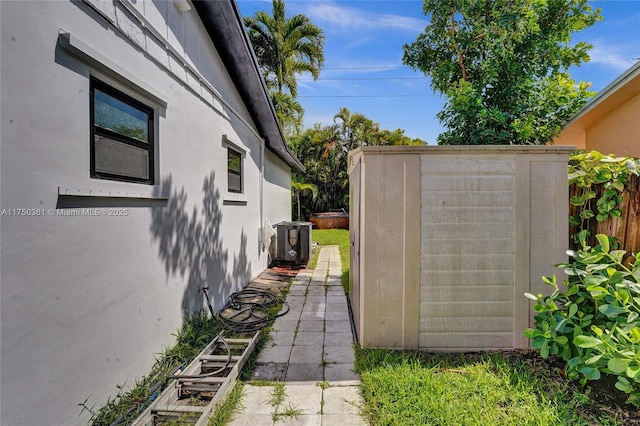 view of side of home with a storage shed, an outbuilding, fence, and stucco siding