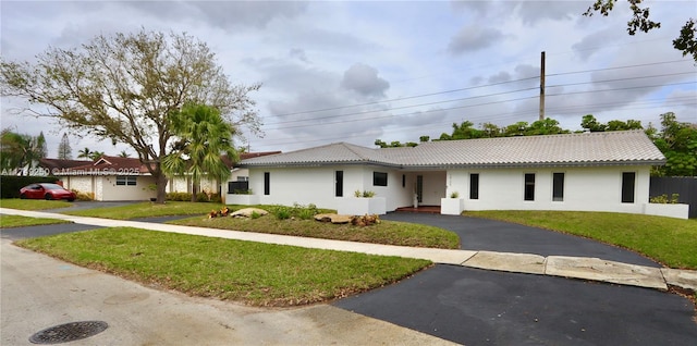 ranch-style house featuring driveway, stucco siding, a tiled roof, and a front yard