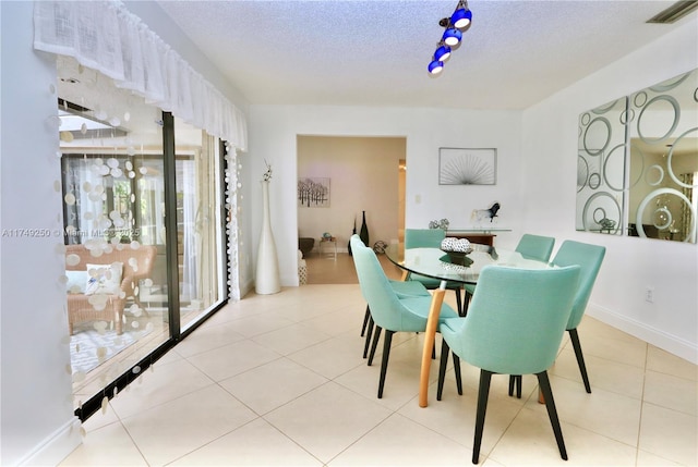 dining area with a textured ceiling, light tile patterned floors, visible vents, and baseboards