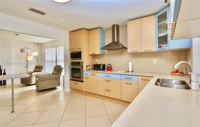 kitchen with stainless steel appliances, a sink, light countertops, wall chimney range hood, and light brown cabinetry