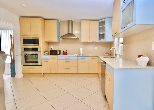 kitchen featuring wall chimney exhaust hood, glass insert cabinets, stainless steel appliances, light countertops, and light brown cabinets