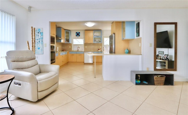 kitchen featuring light tile patterned floors, light brown cabinets, stainless steel appliances, light countertops, and glass insert cabinets