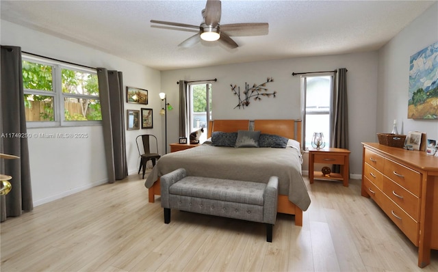 bedroom with ceiling fan, light wood-style flooring, baseboards, and a textured ceiling