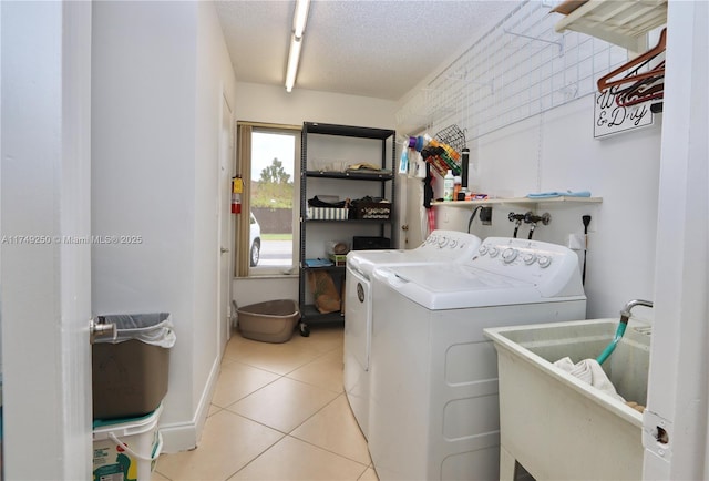 laundry room with washing machine and clothes dryer, light tile patterned floors, a sink, a textured ceiling, and laundry area