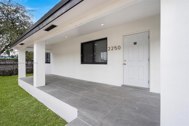 view of exterior entry with fence, a patio, and stucco siding