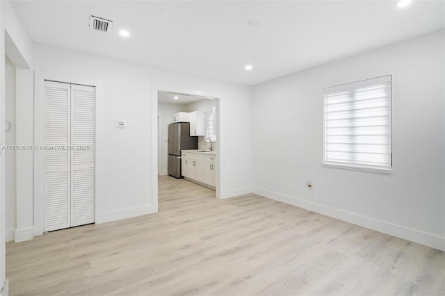 unfurnished bedroom with visible vents, freestanding refrigerator, a sink, light wood-type flooring, and baseboards