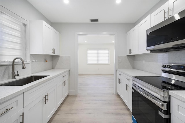 kitchen with stainless steel appliances, a sink, visible vents, white cabinets, and light wood finished floors