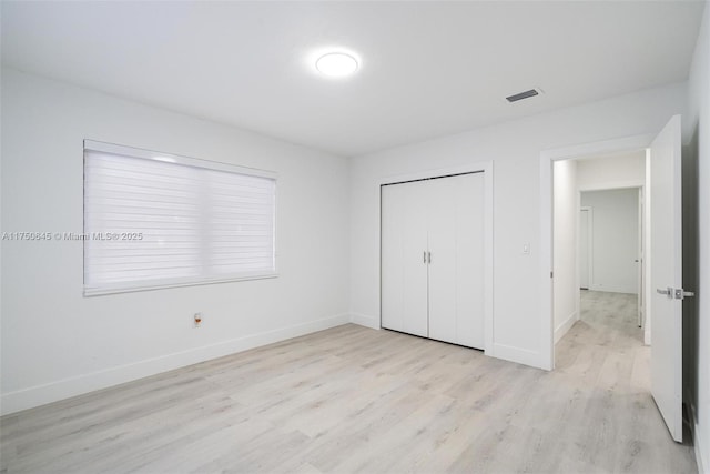 unfurnished bedroom with light wood-type flooring, a closet, visible vents, and baseboards