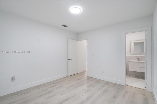 unfurnished bedroom featuring light wood-type flooring, a sink, visible vents, and baseboards