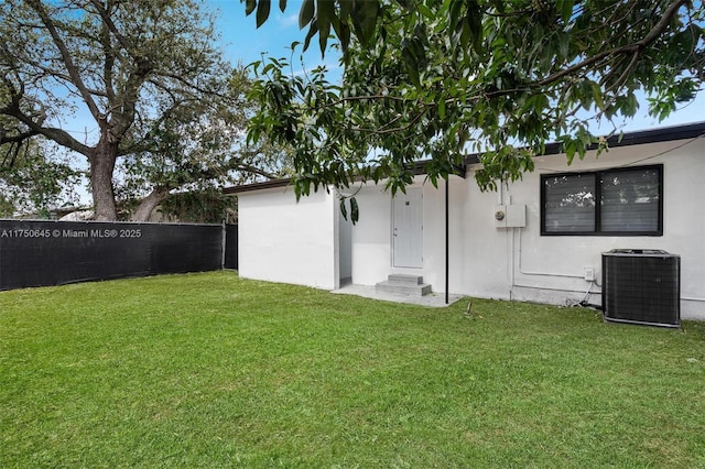 rear view of property featuring stucco siding, a fenced backyard, a yard, and central air condition unit