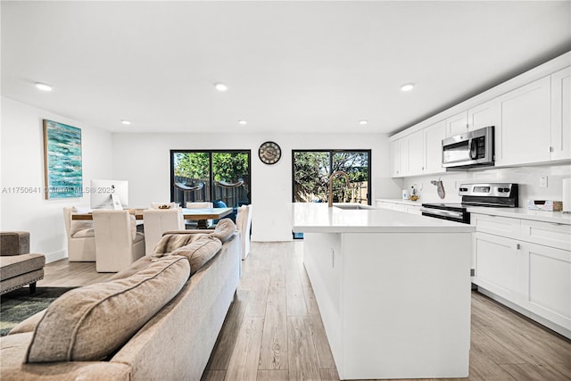 kitchen featuring recessed lighting, light wood-style flooring, appliances with stainless steel finishes, open floor plan, and a sink