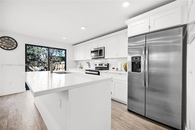 kitchen featuring white cabinets, an island with sink, light wood-style flooring, stainless steel appliances, and a sink