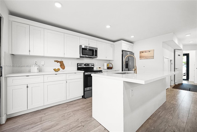 kitchen featuring appliances with stainless steel finishes, a kitchen island with sink, a sink, white cabinetry, and light wood-type flooring