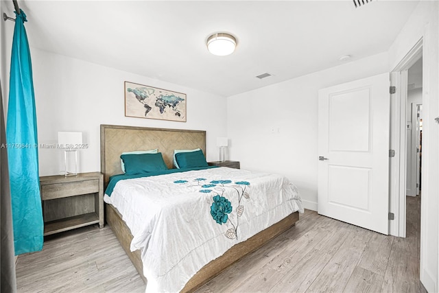 bedroom with baseboards, visible vents, and wood finished floors