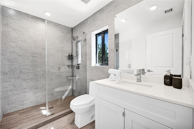 bathroom with visible vents, toilet, wood finished floors, vanity, and a shower stall