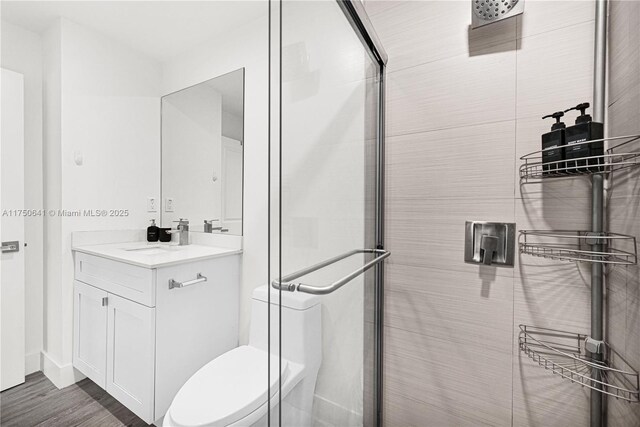 bathroom with a stall shower, vanity, toilet, and wood finished floors