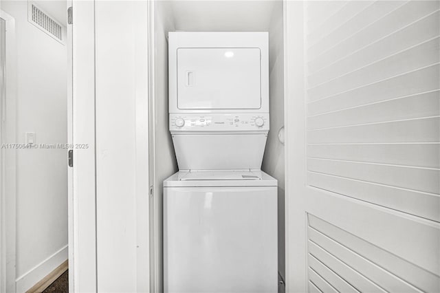 clothes washing area with stacked washer and clothes dryer, visible vents, and laundry area