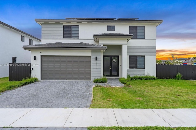 view of front of house with decorative driveway, a front yard, roof mounted solar panels, fence, and a garage