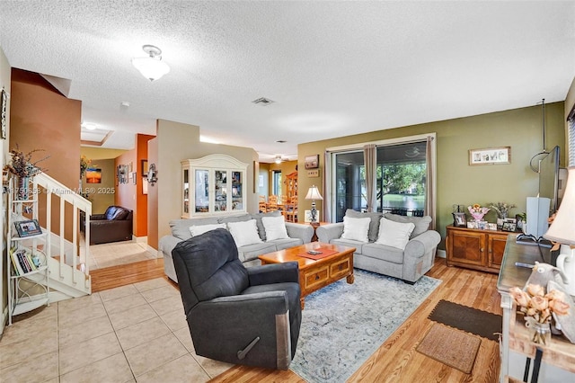 living room featuring light tile patterned floors, visible vents, stairway, and a textured ceiling