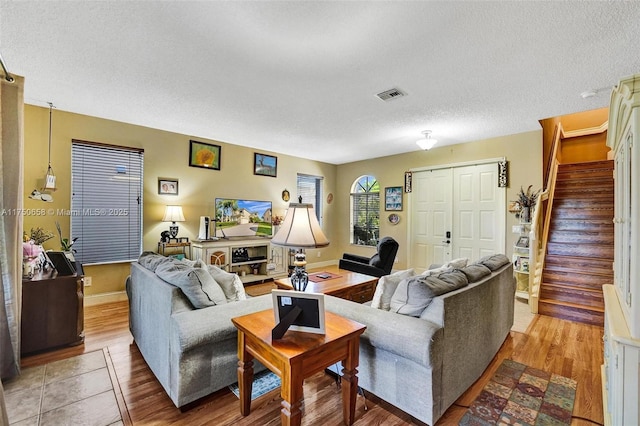 living room featuring a textured ceiling, wood finished floors, visible vents, baseboards, and stairway