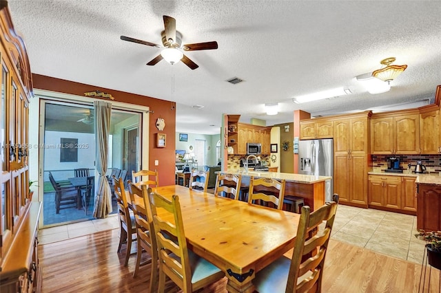 dining space featuring visible vents, ceiling fan, light wood-style flooring, and a textured ceiling