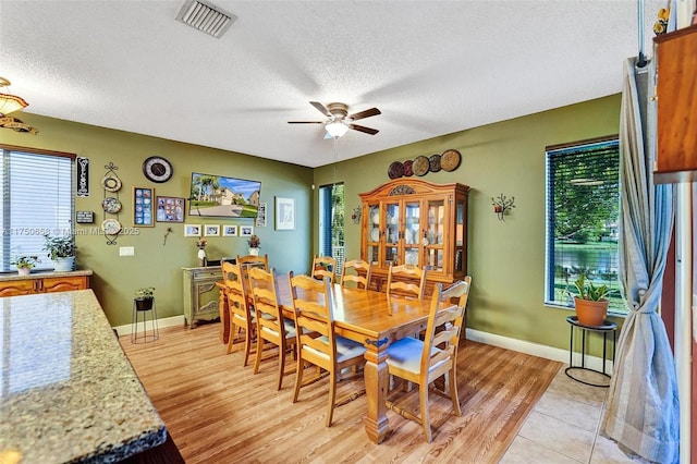 dining room with light wood finished floors, ceiling fan, visible vents, and a textured ceiling