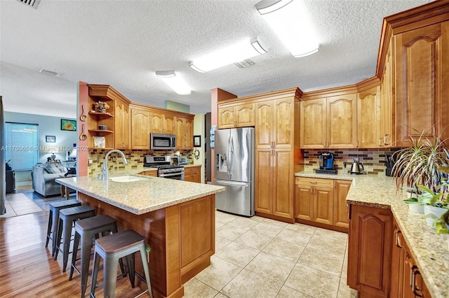 kitchen with open shelves, appliances with stainless steel finishes, a sink, a peninsula, and a kitchen breakfast bar