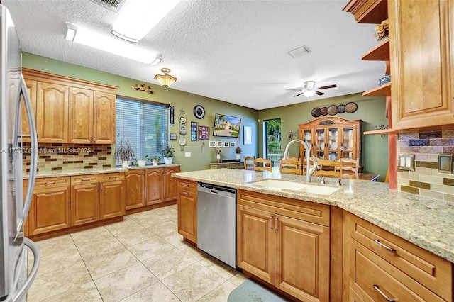 kitchen with appliances with stainless steel finishes, a sink, decorative backsplash, and light stone countertops