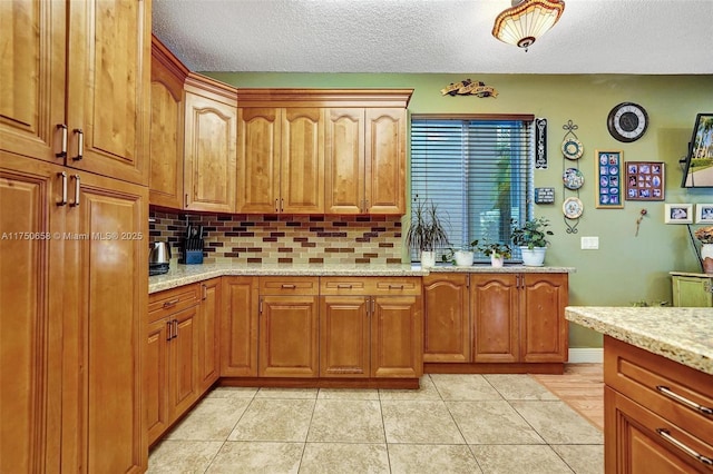 kitchen featuring light tile patterned floors, tasteful backsplash, light stone counters, brown cabinets, and a textured ceiling