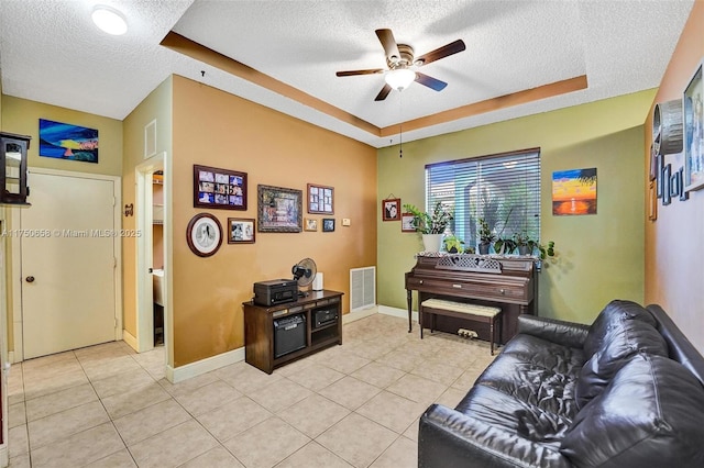 living area with a textured ceiling, a tray ceiling, light tile patterned flooring, and visible vents