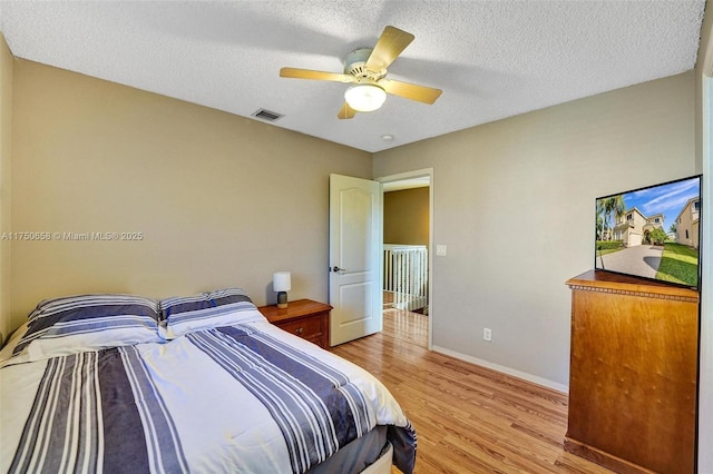 bedroom with baseboards, visible vents, a ceiling fan, a textured ceiling, and light wood-style floors