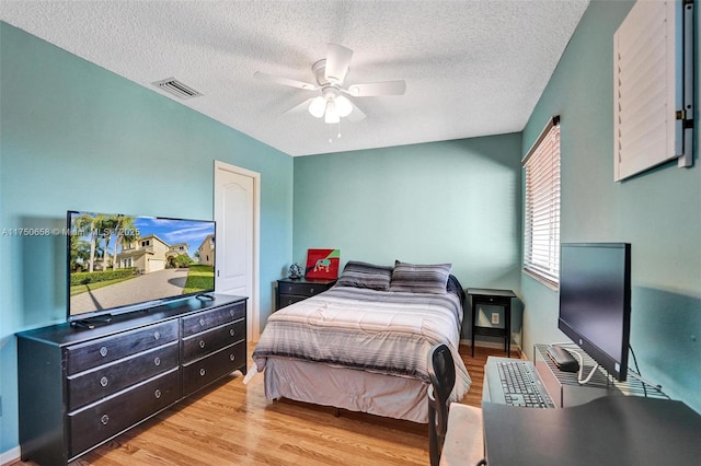 bedroom with a ceiling fan, visible vents, a textured ceiling, and light wood finished floors