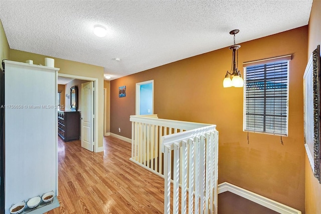 hall featuring light wood finished floors, baseboards, a chandelier, and a textured ceiling